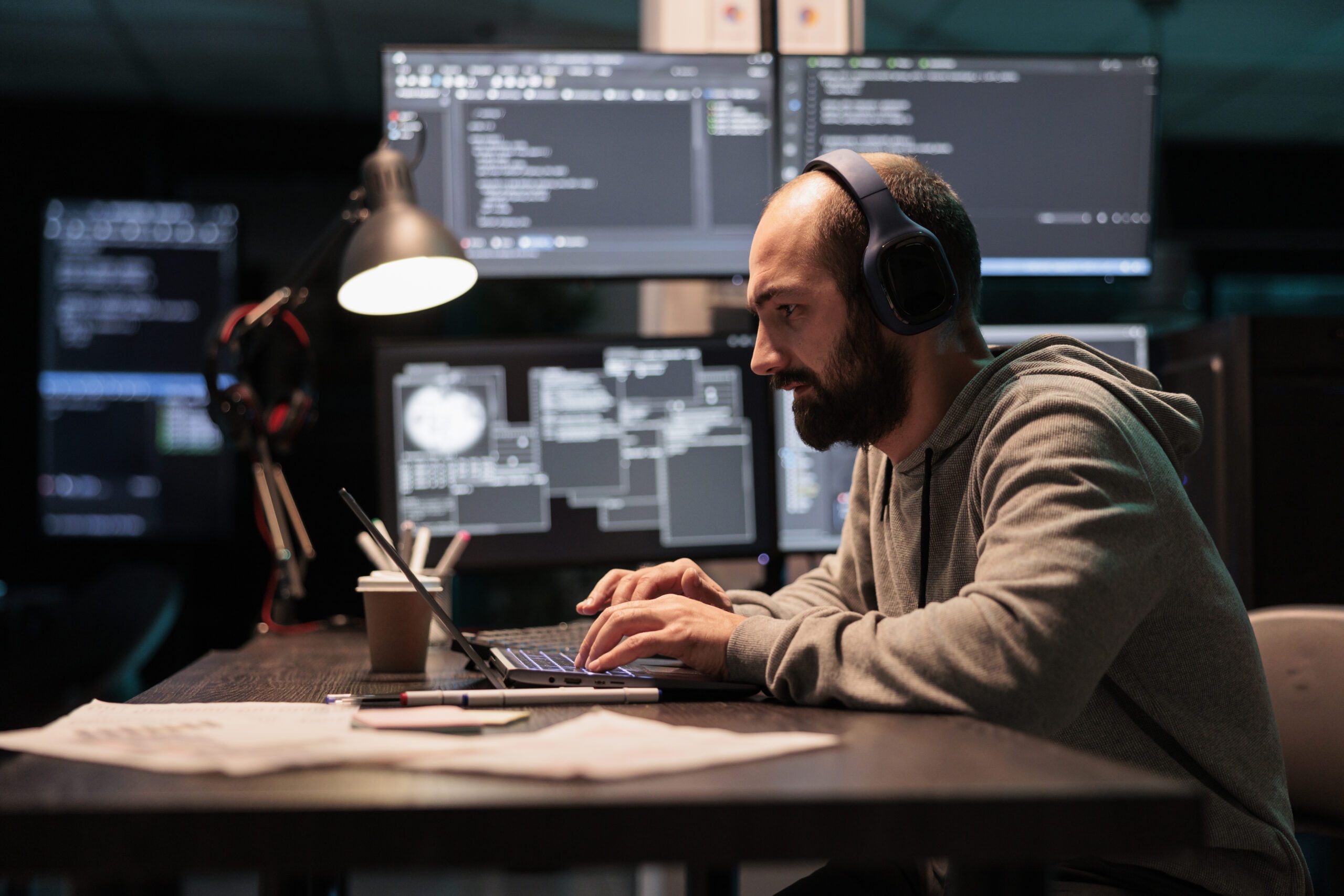 Software engineer typing code on a laptop with multiple monitors