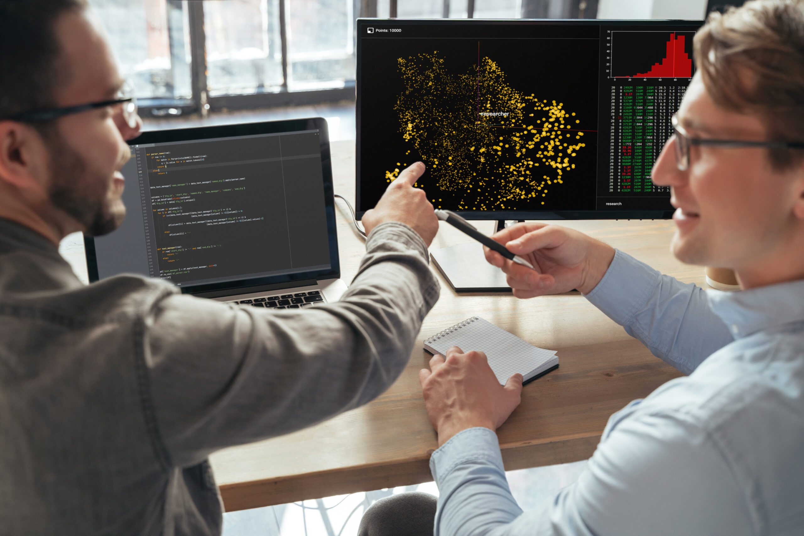 Two colleagues discussing code displayed on monitors