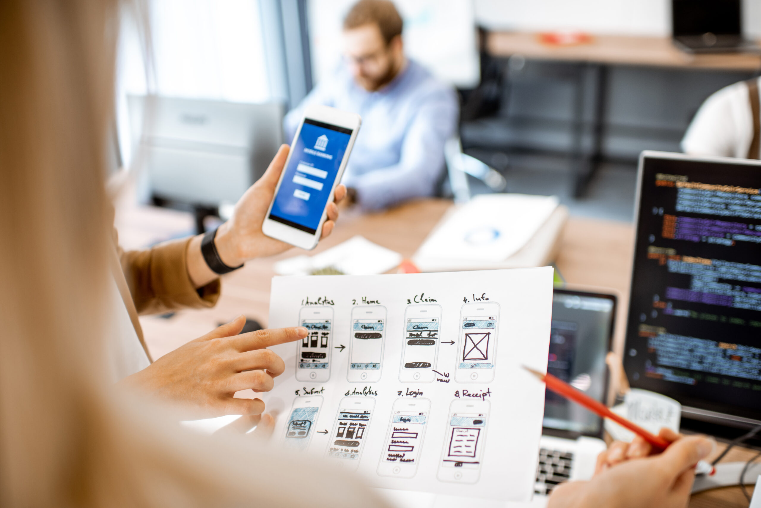 Developers or web designers developing mobile application for banking in the office, close-up on phone and paper sketches