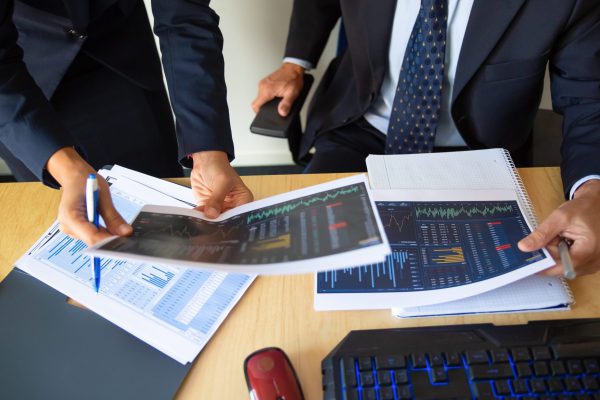 Investor and trader discussing statistic data, holding papers with financial charts and pen. Cropped shot. Broker job or trading concept